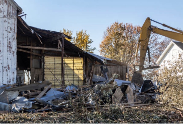 Excavator taking down a weathered barn during a controlled demolition